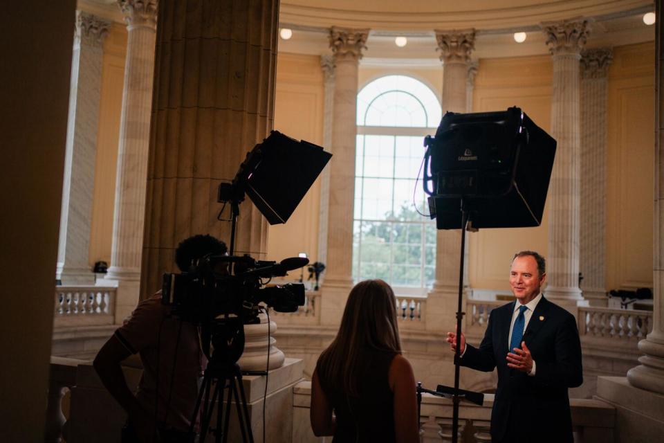 A man with a camera and lights pointed at him speaks