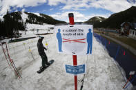 FILE - In this May 27, 2020, file photo, a sign reminds skiers and snowboarders to practice social distancing while wearing a face covering in lift lines at the reopening of Arapahoe Basin Ski Resort, which closed in mid-March to help in the effort to stop the spread of the new coronavirus, in Keystone, Colo. Colorado health officials are weighing in on how to safely navigate the upcoming ski season amid a pandemic as eager skiers and snowboarders who have been cooped up for the greater part of a year prepare to hit the slopes in a matter of weeks. The state released guidance Monday, Oct. 19, after gathering feedback from resorts and county health officials. (AP Photo/David Zalubowski, File)