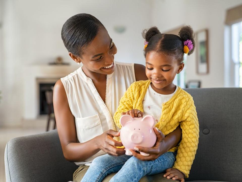 Black woman with daughter holding piggy bank