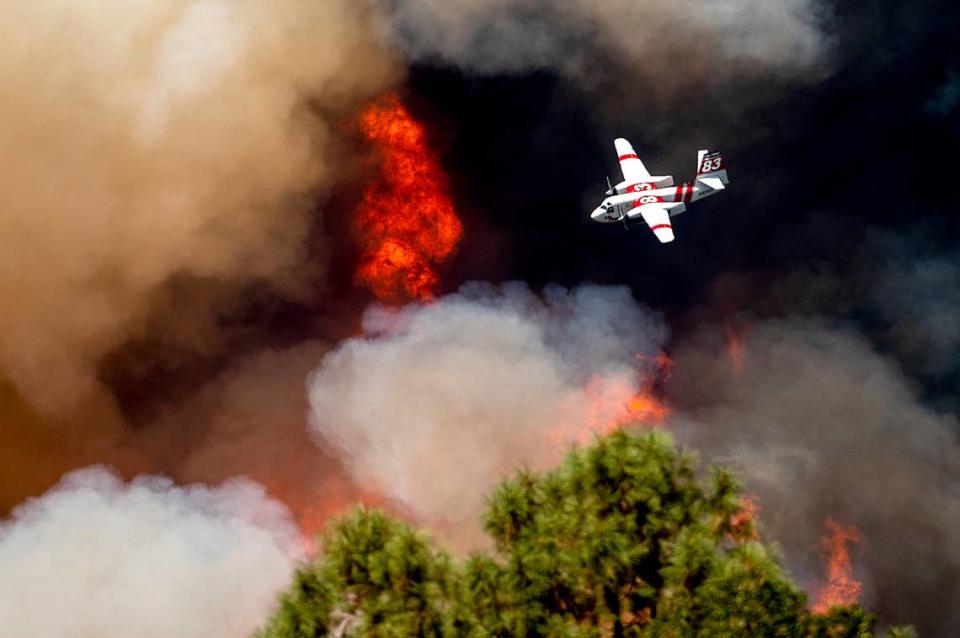 FILE - An air tanker flies past flames while battling the Oak Fire in Mariposa County, Calif., Sunday, July 24, 2022. Wildfires, floods and soaring temperatures have made climate change real to many Americans. Yet a sizeable number continue to dismiss the scientific consensus that human activity is to blame. That’s in part because of a decades-long campaign by fossil fuel companies to muddy the facts and promote fringe explanations. (AP Photo/Noah Berger, File)