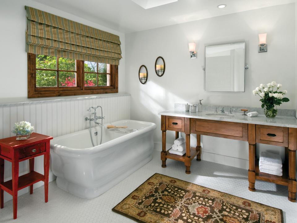 A white bathroom with a tub on the left and a wooden vanity with a marble countertop and sink on the right