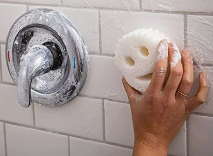 Person's hand using a Scrub Daddy sponge with the Scrub Daddy cleaning paste on a shower wall