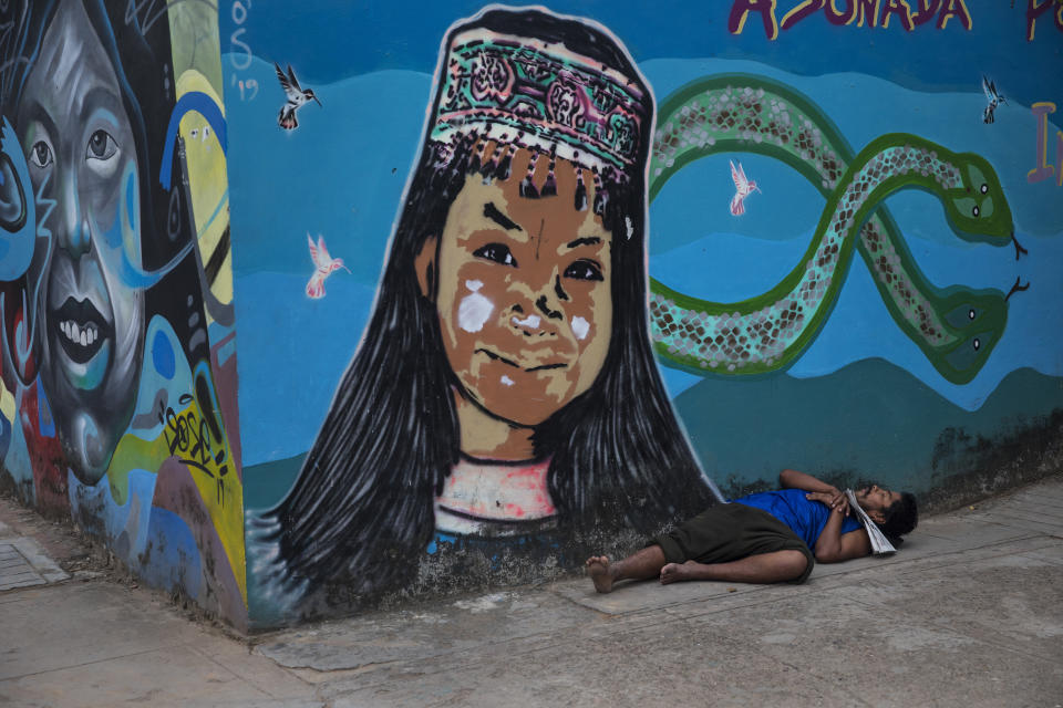 A homeless man sleeps against a wall adorned with a mural featuring a Shipibo Indigenous girl and Amazon rainforest animals, in Pucallpa, in Peru's Ucayali region, Wednesday, Sept. 2, 2020. Peru is home to one of Latin America's largest Indigenous populations, whose ancestors lived in the Andean country before the arrival of Spanish colonists. (AP Photo/Rodrigo Abd)