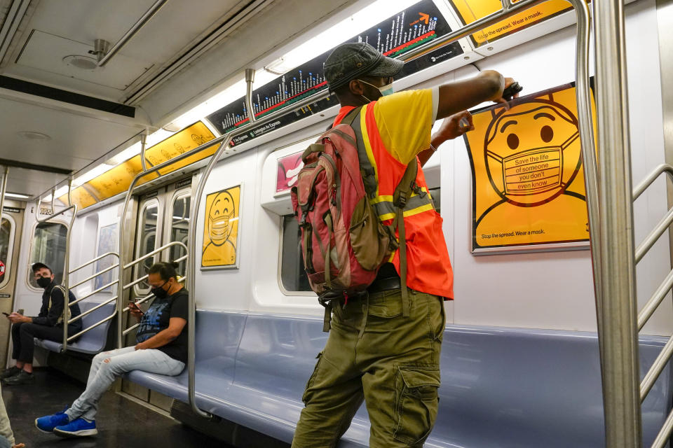 An MTA employee replaces posters reminding commuters to wear face masks in a subway car, Monday, Sept. 14, 2020, in the Brooklyn borough of New York. The Metropolitan Transportation Authority announced a new public service campaign to encourage mask usage as well as a new $50 fine policy for those who refuse to wear face coverings on subways, buses and commuter railroads. (AP Photo/Mary Altaffer)