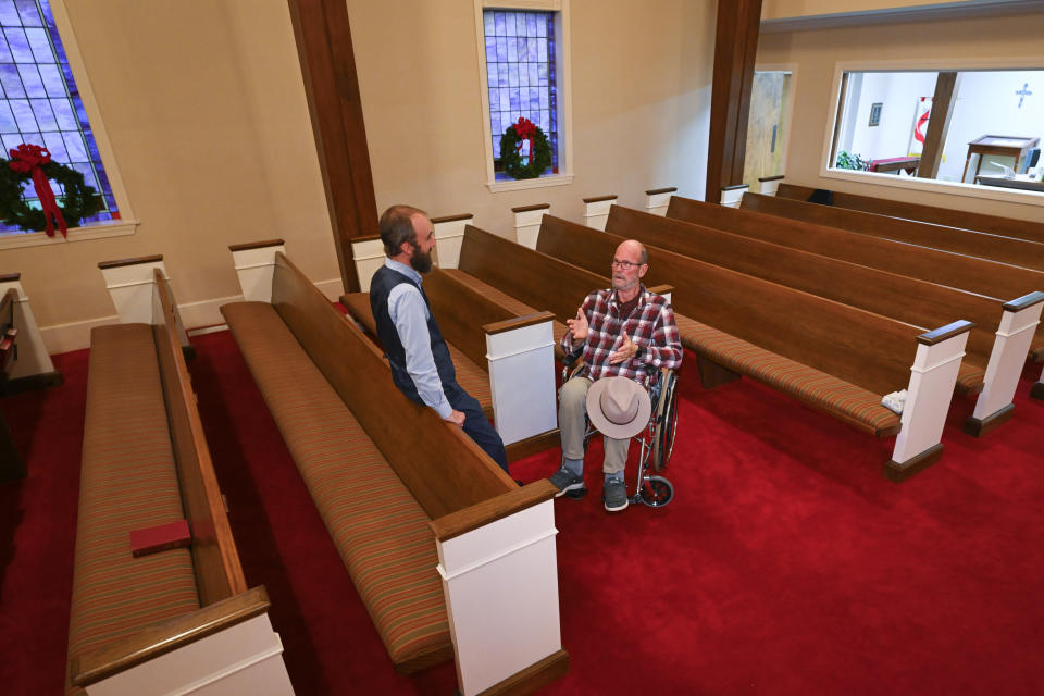 Jerry Lamb, who suffers from a spine condition, talks to Pastor Adam Kelchner at Camden First United Methodist Church Thursday, Dec. 8, 2022, in Camden, Tenn. The church at the urging of the pastor recently had a couple pews cut in half so Jerry, and anyone else who uses a wheelchair, walker or other aid, can still sit with the rest of the congregation. (AP Photo/John Amis)