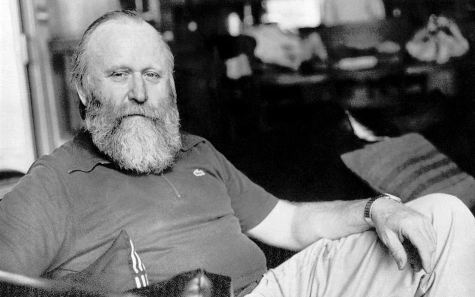 Black and white photograph of a bearded man sitting in a chair and posing for the camera.