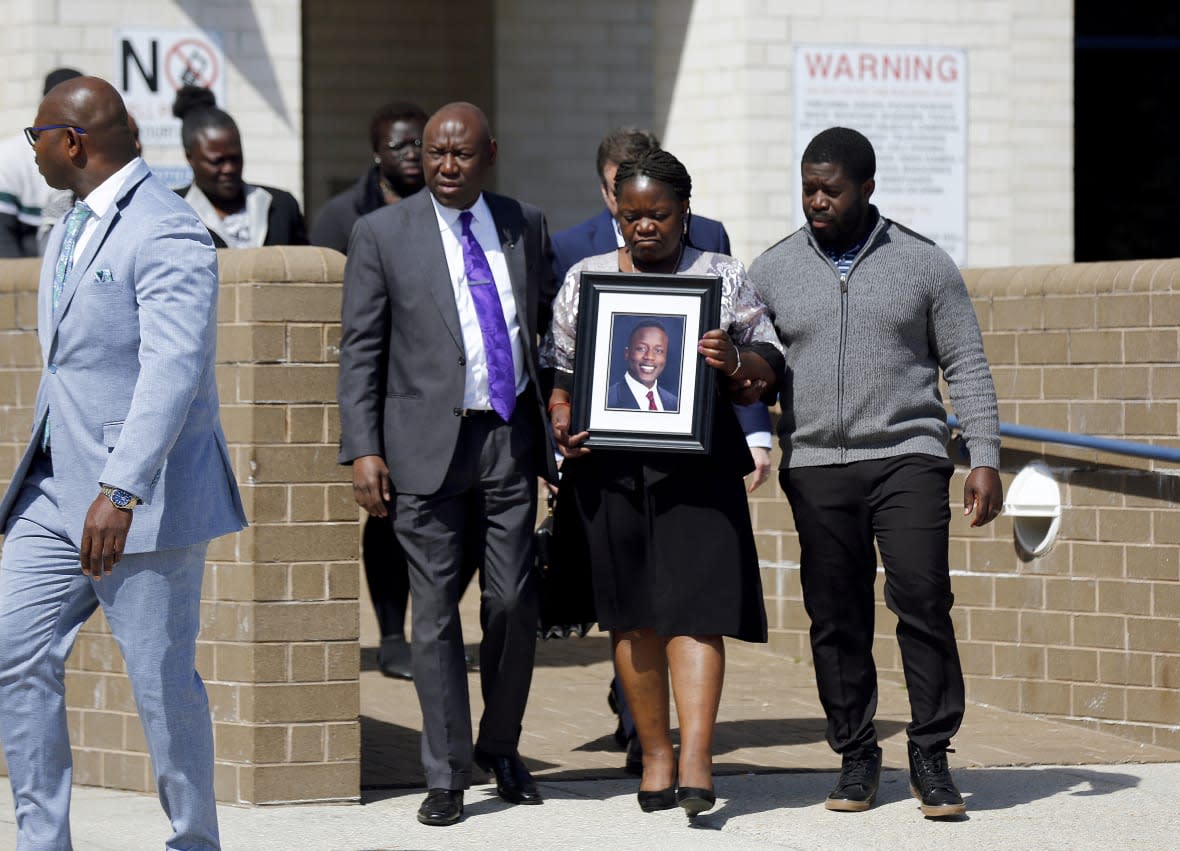 Caroline Ouko, mother of Irvo Otieno, holds a portrait of her son as she walks out of the Dinwiddie Courthouse with attorney Ben Crump, center left, and her older son, Leon Ochieng, in Dinwiddie, Va., on Thursday, March 16, 2023. (Daniel Sangjib Min/Richmond Times-Dispatch via AP)