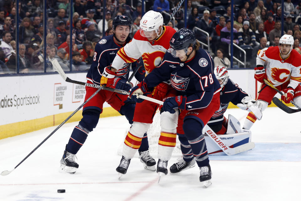 Calgary Flames forward Yegor Sharangovich, center, reaches for the puck between Columbus Blue Jackets defensemen Zach Werenski, left, and Damon Severson during the first period of an NHL hockey game in Columbus, Ohio, Friday, Oct. 20, 2023. (AP Photo/Paul Vernon)