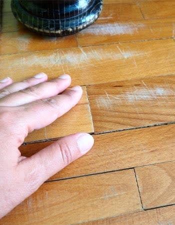 A close up of a hand touching a hardwood floor plank.
