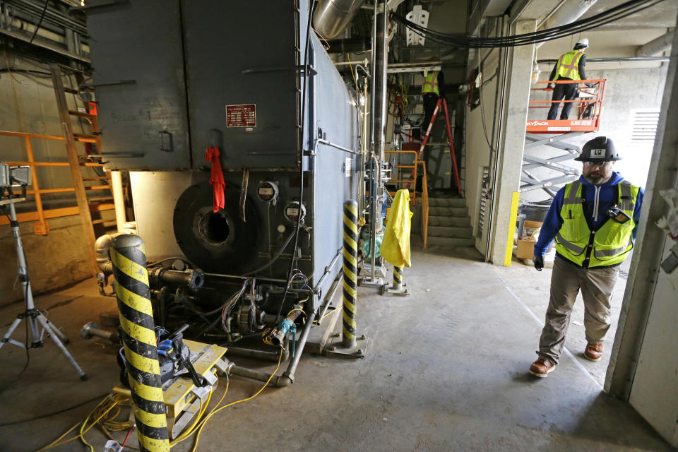 In this March 16, 2017 photo, Bryan Troupe, right, a safety officer at the West Point Treatment Plant in Seattle, walks through an area where workers were repairing a boiler and stringing temporary power sources after the room was flooded nearly to the ceiling during a massive equipment failure. The county-run facility has been hobbling along at about half-capacity since the Feb. 9 electrical failure resulted in catastrophic flooding that damaged an underground network of pumps, motors, electric panels and other gear. (AP Photo/Ted S. Warren)