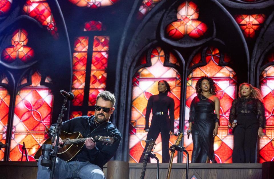 A guitarist performs with three backup singers behind him.