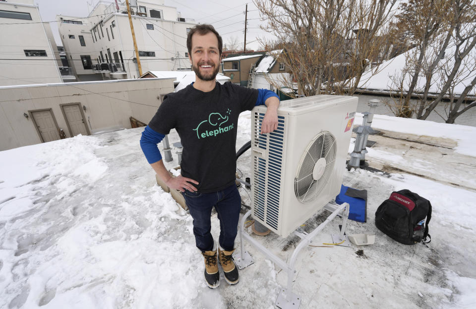 David Richardson, co-founder of Elephant Energy, leans on the condenser placed on the roof during the installation of a heat pump in an 80-year-old rowhouse Friday, Jan. 20, 2023, in northwest Denver. (AP Photo/David Zalubowski)