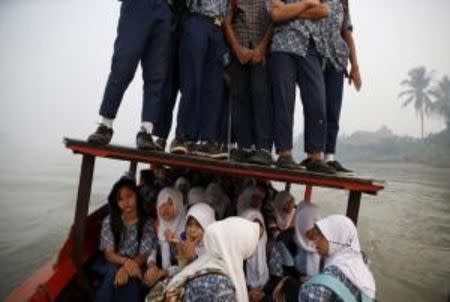 Students stand on the roof of a wooden boat as haze blankets the Musi River while they travel to school in Palembang, on Indonesia's Sumatra island, September 10, 2015. REUTERS/Beawiharta