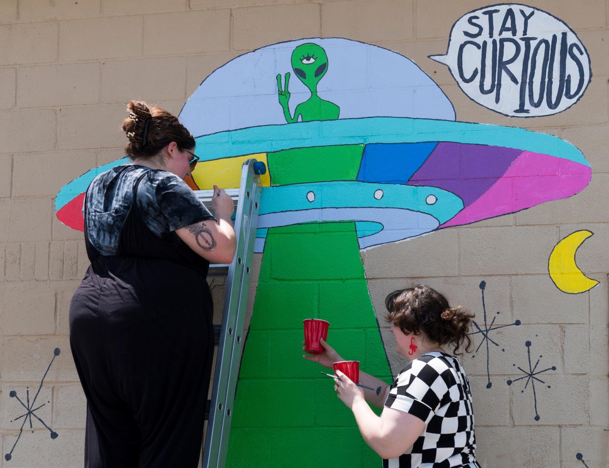 Owners Jasmine Elzy, left, and Kyla Ford, right, work on a  new mural outside their shop Corkscrew Curiosities in Henderson, Ky., Thursday, May 12, 2022.