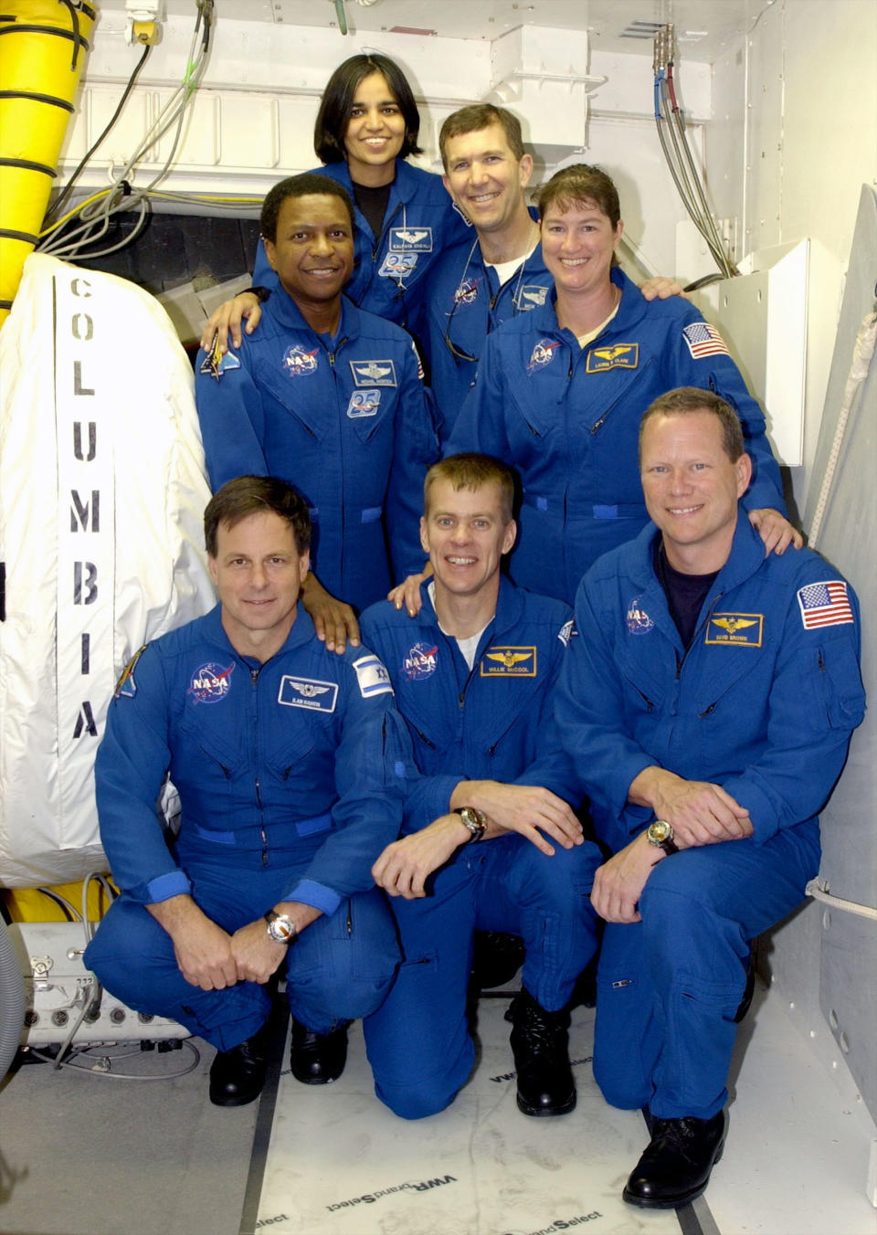 Die STS-107-Besatzung posiert vor der Luke des Space Shuttle Columbia.  Vorne kniend (von links nach rechts): Nutzlastspezialist Ilan Ramon, Pilot Willie McCool und Missionsspezialist David Brown.  Hinten stehen: die Missionsspezialisten Michael Anderson und Kalpana Chawla, Commander Rick Husband und Missionsspezialistin Laurel Clark.