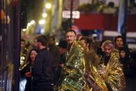 People warm up under protective thermal blankets as they prepare to board a bus to be evacuated near the Bataclan concert hall following fatal attacks in Paris, France, November 14, 2015. REUTERS/Christian Hartmann