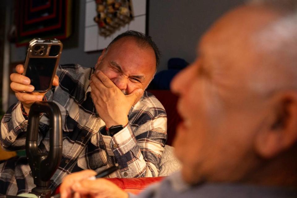 Carlos Olives III laughs and his listens and records video interviews while his father Carlo Jr. tells stories at home in Sacramento on Friday, March 22, 2024. His son Carlos said it took more than a year for the cause of his father’s dementia – Alzheimer’s disease – to be diagnosed. Since getting the diagnosis, a specialist has prescribed medications to improve Carlos Sr.’s memory, attention and mood.