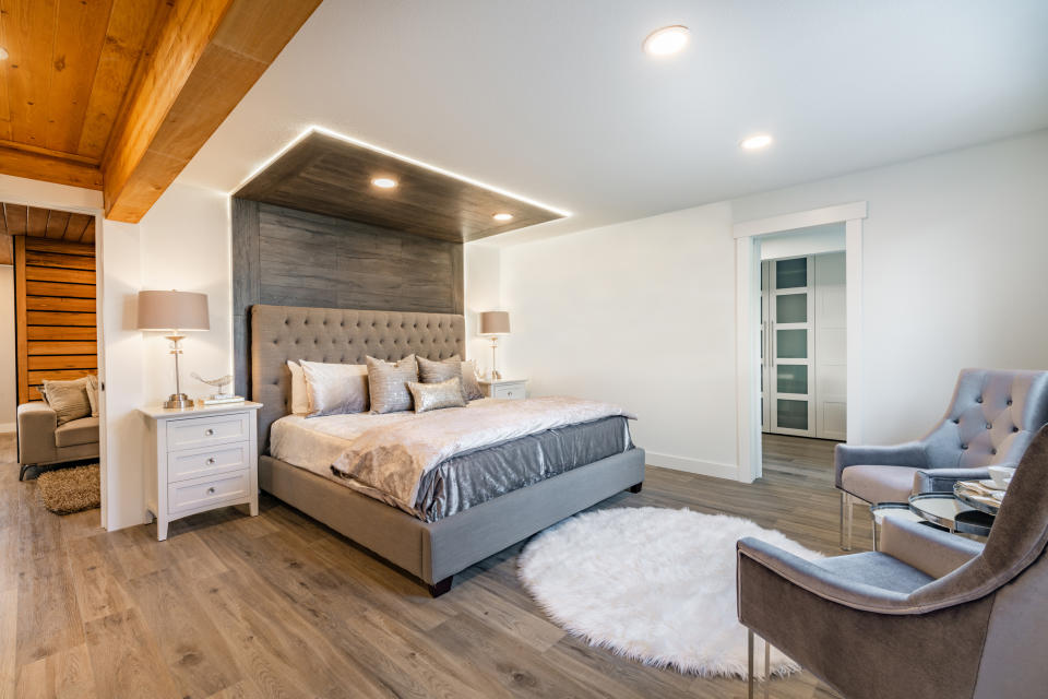 Modern bedroom with a tufted headboard bed, nightstands, lamps, cozy seating area, round rug, wood flooring, and recessed lighting