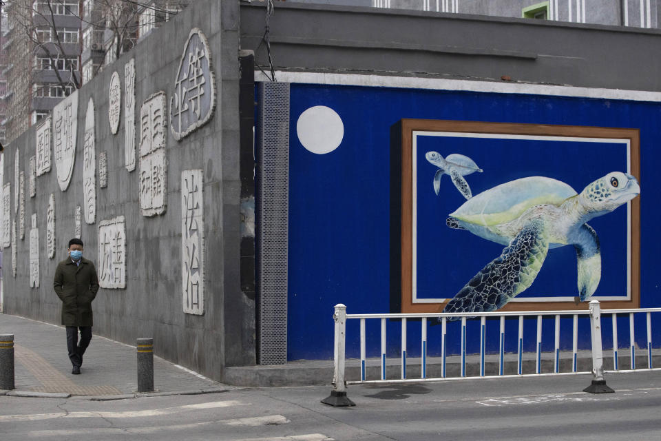 A resident wearing mask walks near a mural outside a school that's closed in Beijing, China on Tuesday, Feb. 25, 2020. The new virus took aim at a broadening swath of the globe Monday, with officials in Europe and the Middle East scrambling to limit the spread of an outbreak that showed signs of stabilizing at its Chinese epicenter but posed new threats far beyond. (AP Photo/Ng Han Guan)