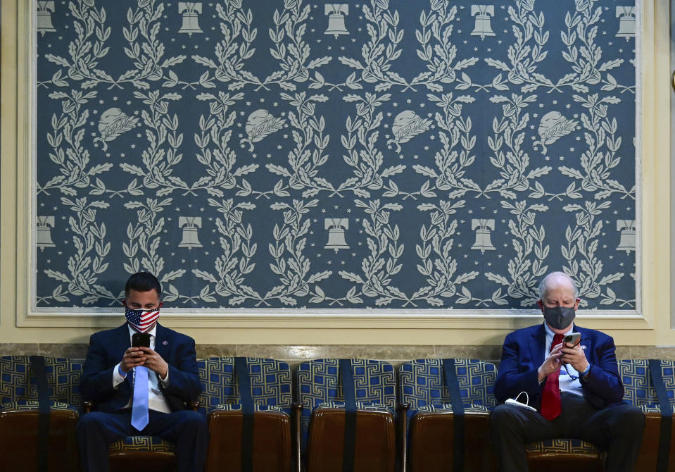 Two members of Congress look at their phones as they sit apart, socially distanced, ahead President Joe Biden's address to a joint session of Congress, Wednesday, April 28, 2021, in the House Chamber at the U.S. Capitol in Washington. (Jim Watson/Pool via AP)