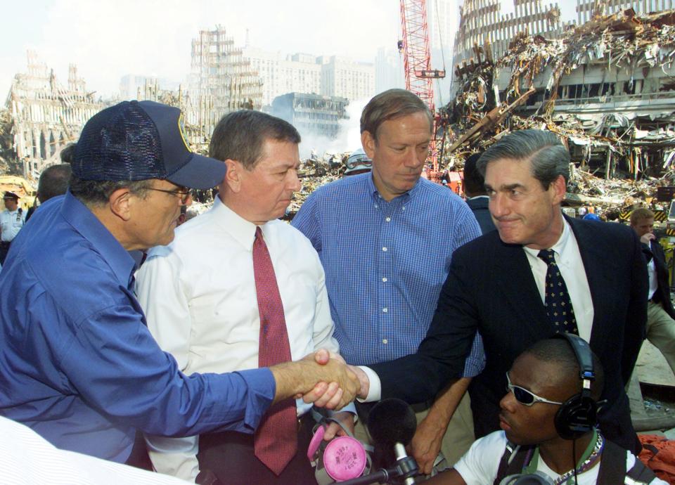 <p>FBI Director Robert Mueller (R) shakes hands with New York Mayor Rudolph Giuliani (L) at the World Trade Disaster site in New York 21 September 2001. Attorney General John Ashcroft (2nd L), accompanied by Mueller and New York Governor George Pataki (2nd R), got a firsthand look at the World Trade Center devastation and promised to rebuild New York. (Photo: Mike Segar/AFP/Getty Images) </p>