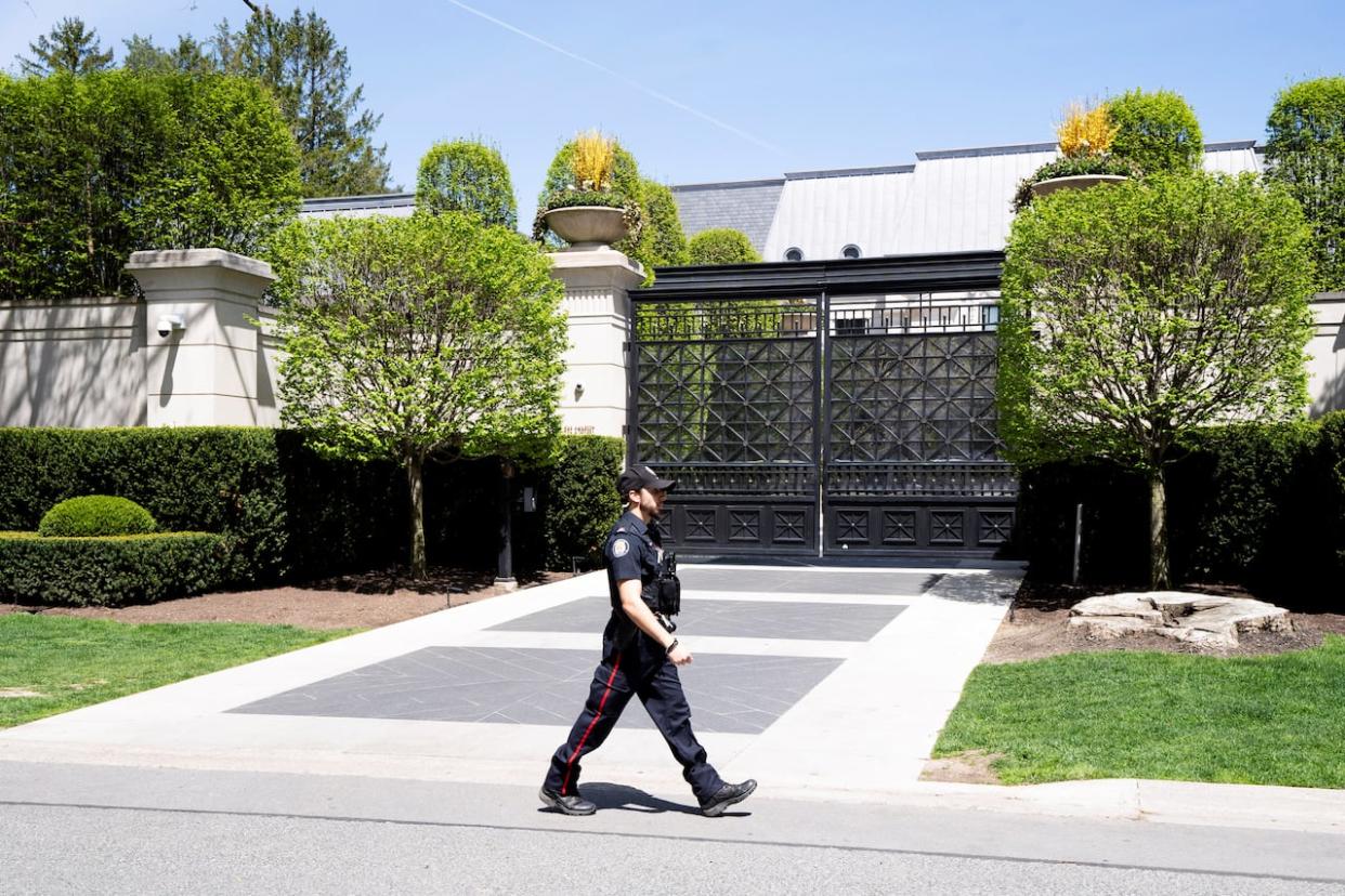 A Toronto police officer walks outside Drake's Bridle Path mansion after a security guard was shot on Tuesday.  (Arlyn McAdorey/Reuters - image credit)