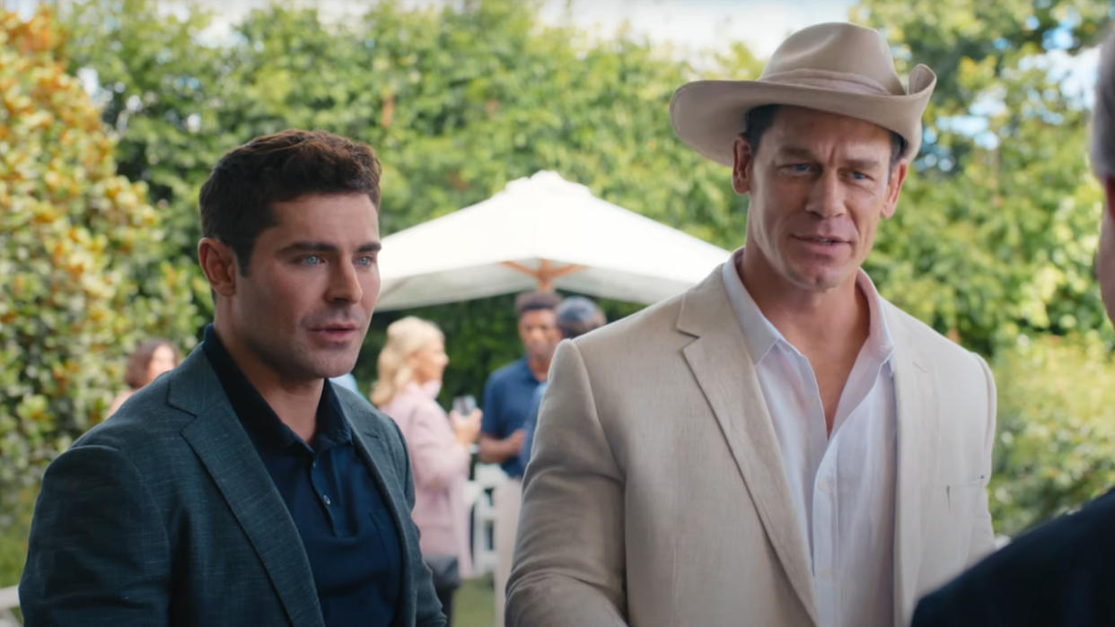  Zac Efron and John Cena standing together in conversation at a party in Ricky Stanicky. 