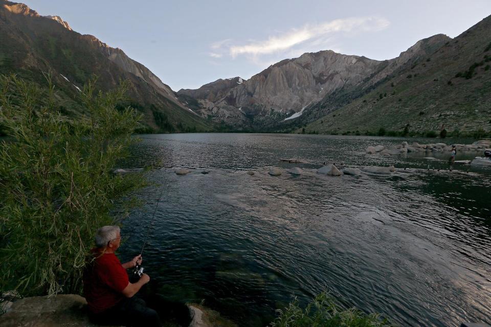 A man casts a fishing line into a mountain lake.