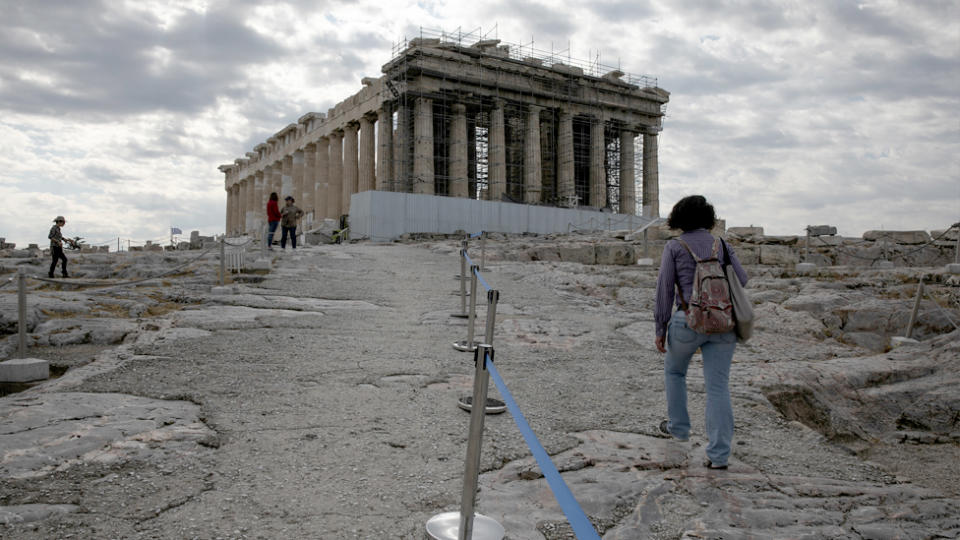 An employee of the Greek Culture ministry walks alongside a retractable belt separating visitors at the archaeological site of the Acropolis.