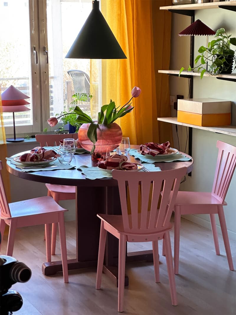 Pink dining chairs surround a round dining table adorned with tulip garlands.