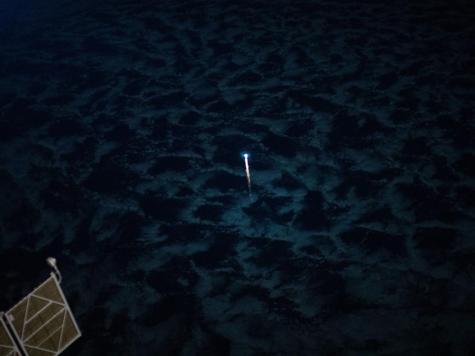 bright rocket streak rises in the distance above deep blue and black nighttime clouds