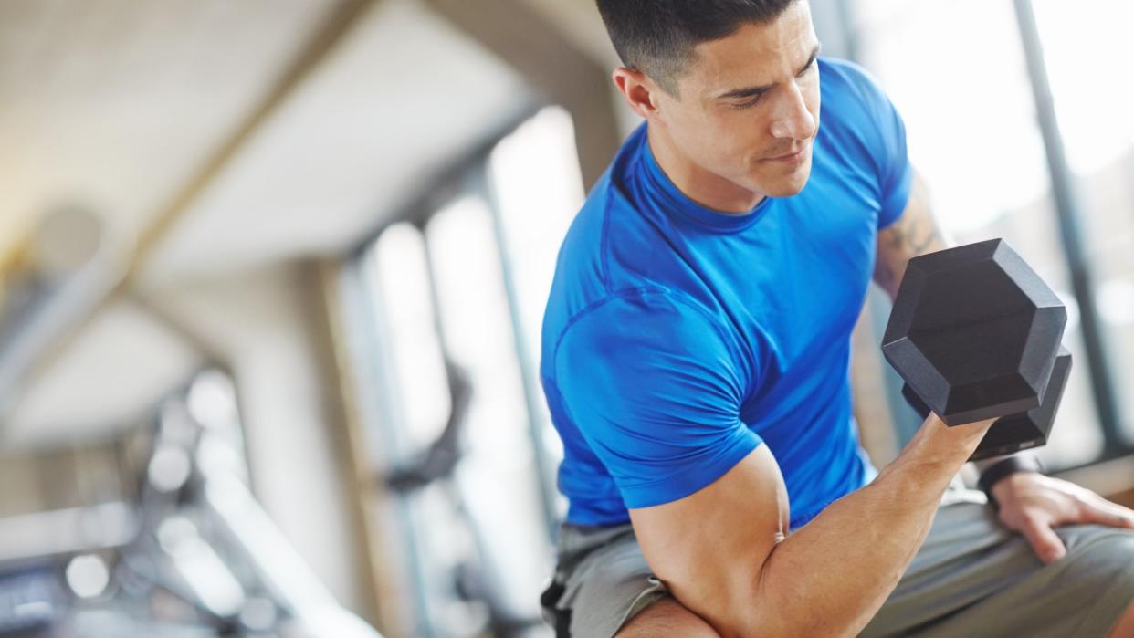  Man performing a bicep curl with elbow against knee using dumbbell during arm workout 