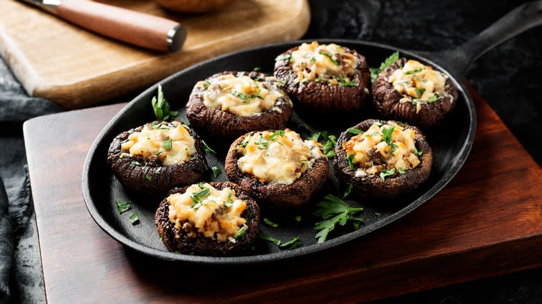 meat and cheese stuffed mushrooms on a dark plate over wood