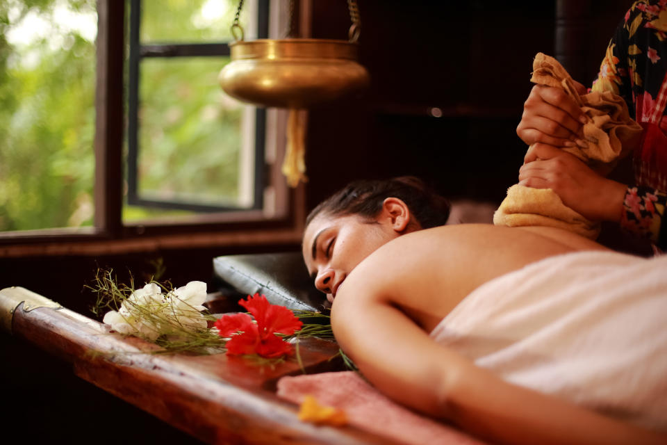 Female therapist treating a young lady in an ayurvedic spa following Indian traditional method.