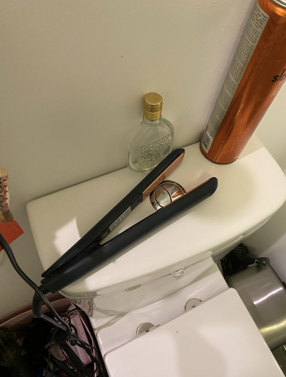 A hot curling iron has been placed so that it's surrounding the button on top of the toilet that has to be pressed to flush it