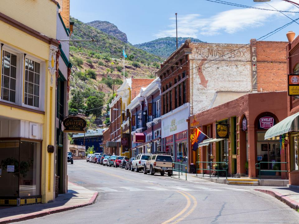 A street lined with cars and shops in Bisbee, arizona with mountains in the background