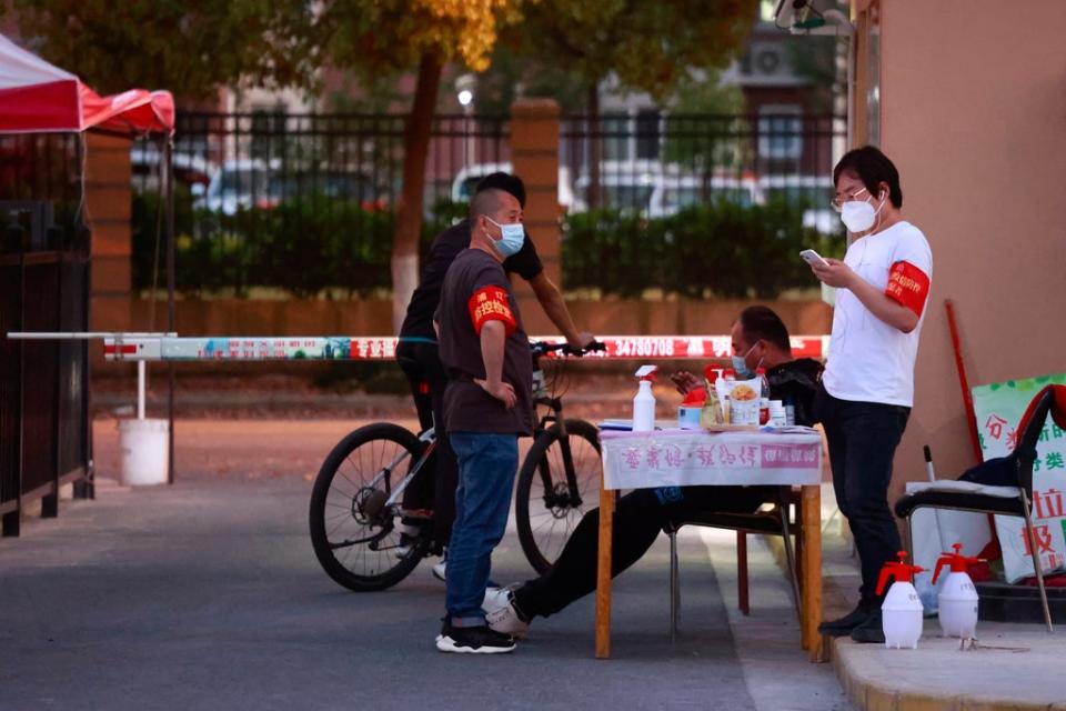 Volunteers wearing armbands and face masks stand at the gate of a residential community in Shanghai, China (AP)