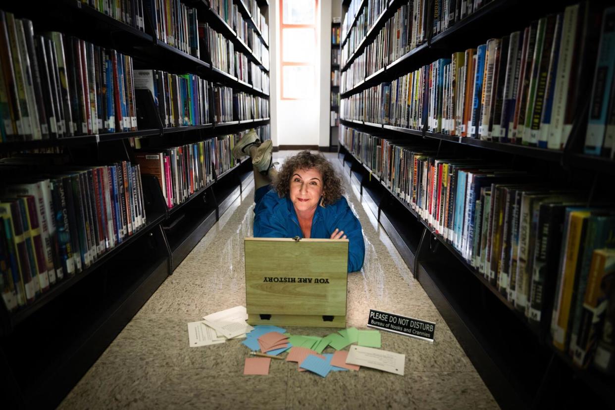 Puzzle designer Andy Crocker sits between bookshelves with the immersive puzzle at the Atwater Village branch library.