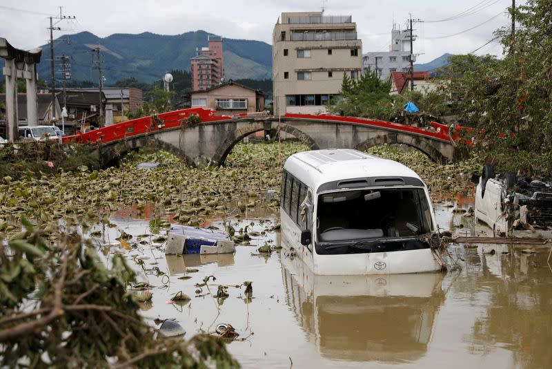 A broken bridge is seen in the back, as an overturned vehicle and a partially submerged bus are pictured in floodwaters caused by torrential rain in Hitoyoshi, Kumamoto Prefecture