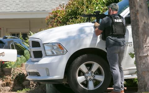 A San Diego Police officer keeps aim on the house thought to be the home of 19 year-old John T. Earnest, who is a suspect in the shooting of several people in a Poway synagogue - Credit: AP