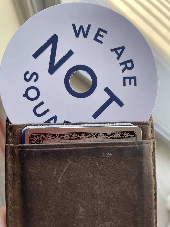 A wallet with cards inside and a partially visible circular sign reading "We Are Not Square."