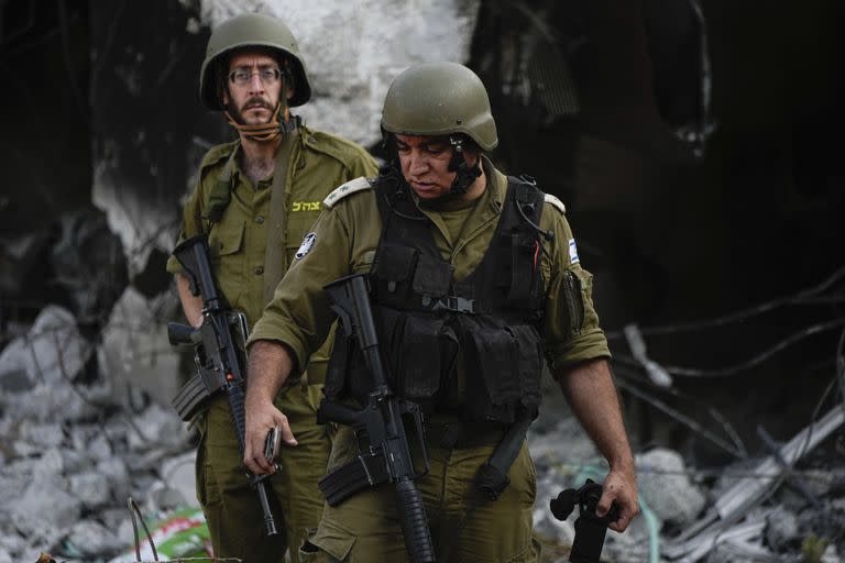 Soldados israelíes pasan junto a casas destruidas por milicianos de Hamas en el kibbutz Be'eri, Israel, el sábado 14 de octubre de 2023