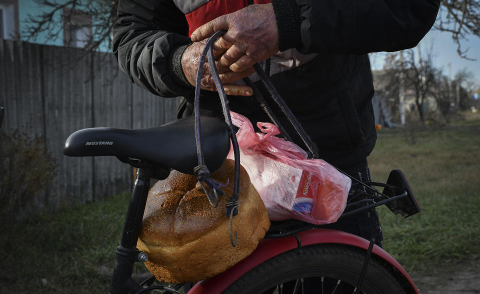 A local resident secures food on bicycle after receiving it at a mobile humanitarian aid point in the village of Zarichne, Donetsk region, Ukraine, Friday, Dec. 2, 2022. (AP Photo/Andriy Andriyenko)