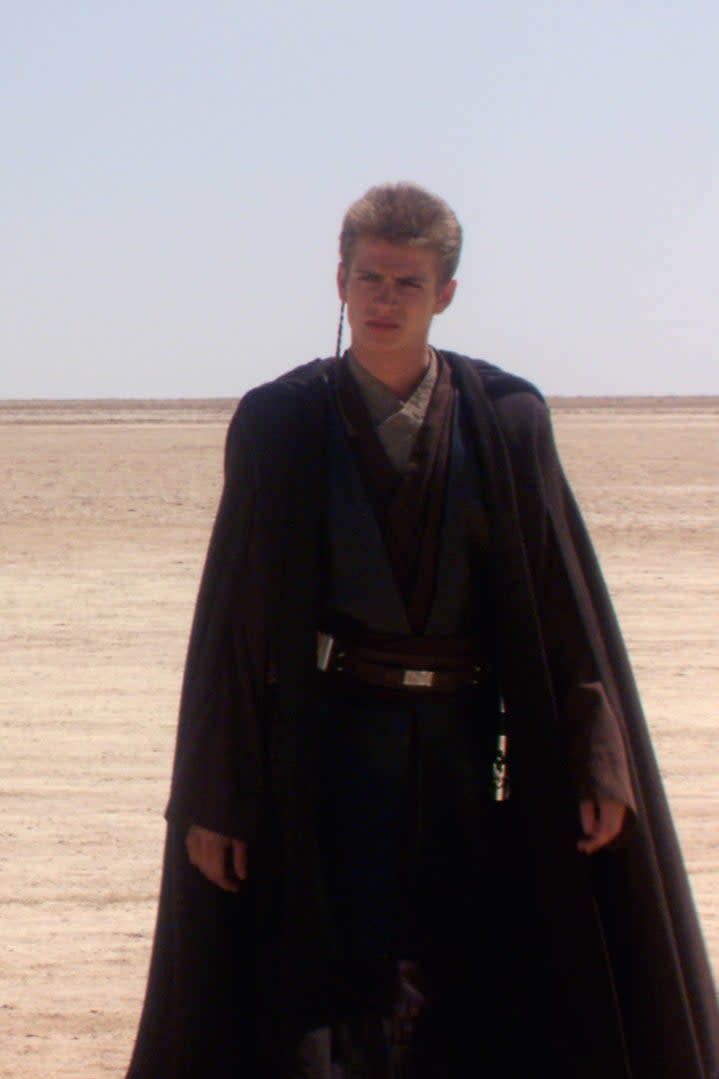 Padmé Amidala in a hooded cloak, Anakin Skywalker in a dark robe, and R2-D2 in a desert scene from Star Wars