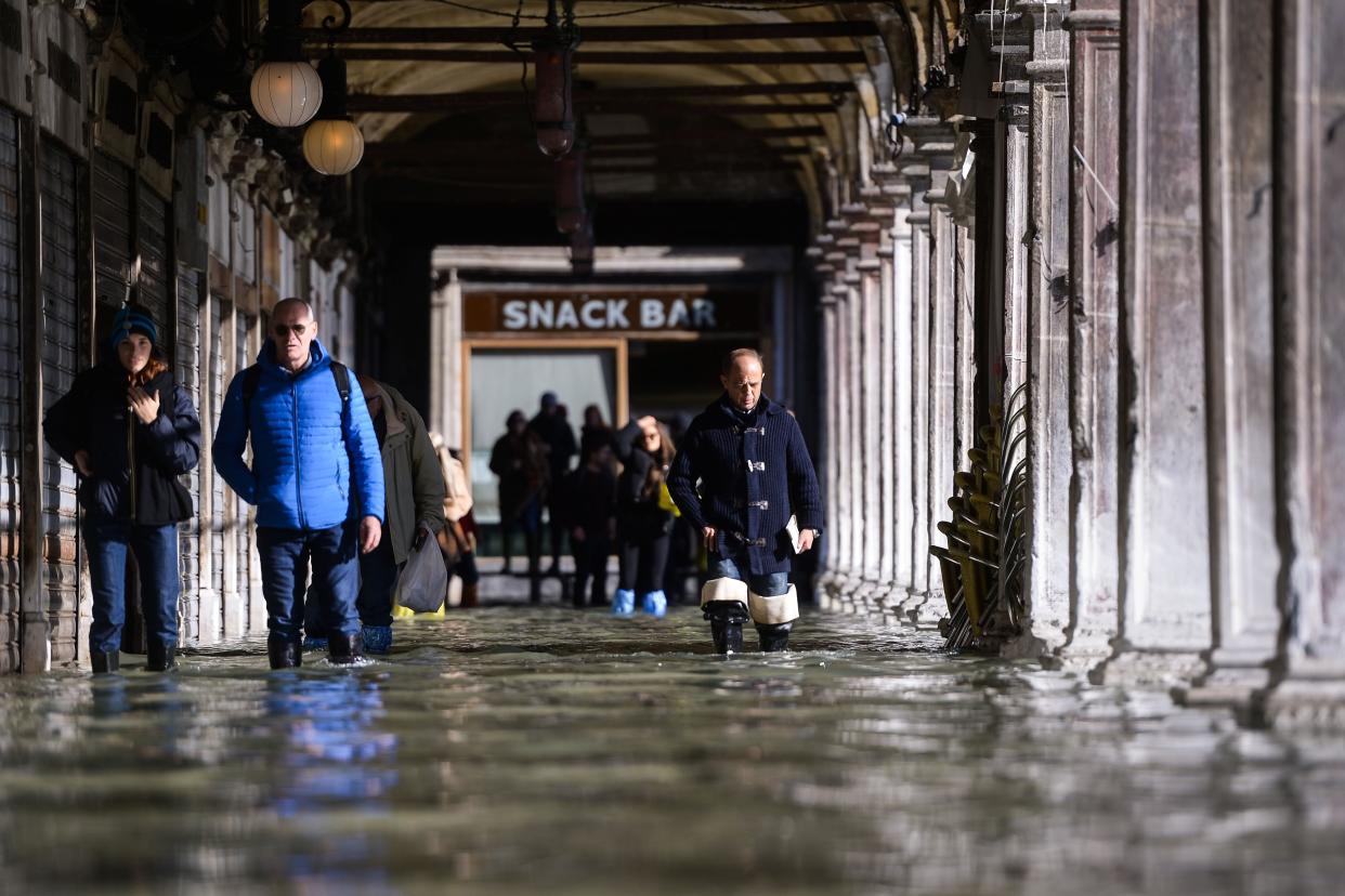 People walk across a floodedarcade by St. Mark's Square on November 14, 2019 in Venice. Much of Venice was left under water after the highest tide in 50 years ripped through the historic Italian city, beaching gondolas, trashing hotels and sending tourists fleeing through rapidly rising waters. 