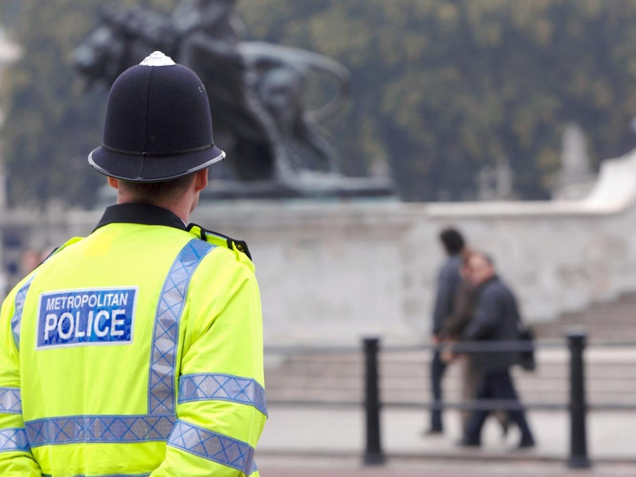 A British police man stands on duty across the road from Buckingham Palace, as tourists pass by in the background on their way to see the Changing of the Guard.