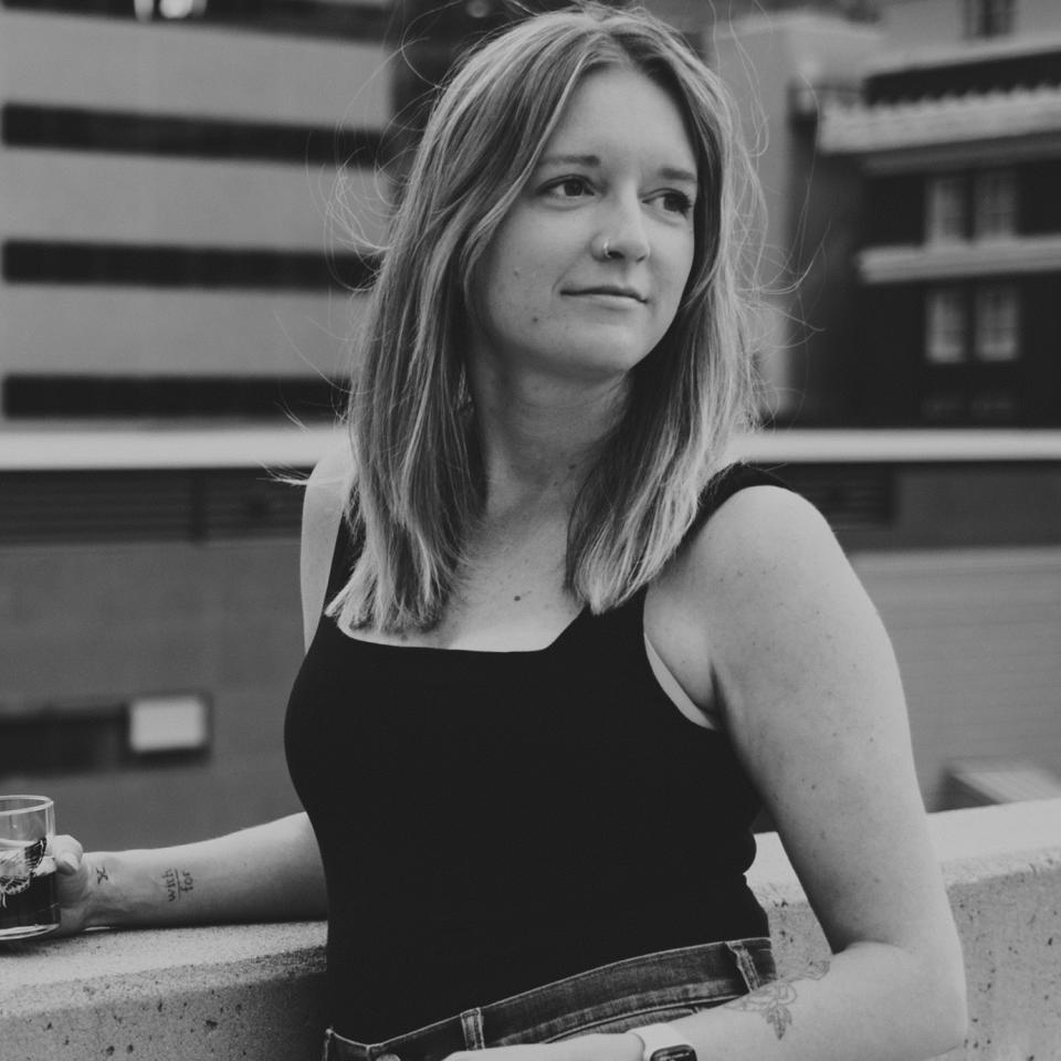 Person holding a cup, seated outdoors with a thoughtful expression, in a casual sleeveless top