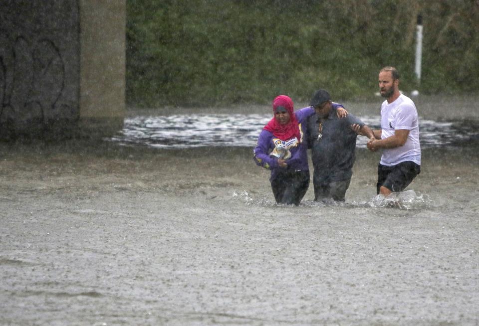 FILE - A man helps two people walk through flood water after their car got stuck on Vandeventer Avenue underneath Interstate-64 in St. Louis, Mo., July 28, 2022. Costly weather disasters kept raining down on America last year, pounding the nation with 18 climate extremes that caused at least $1 billion in damage each, totaling more than $165 billion, federal climate scientists calculated Tuesday, Jan. 10, 2023. (Allie Schallert/St. Louis Post-Dispatch via AP, File)