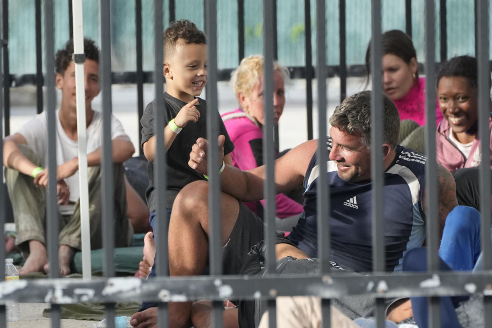 A young boy plays with recently arrived migrants as they wait in a garage area of the U.S. Customs and Border Protection - Marathon Border Patrol Station, Wednesday, Jan. 4, 2023, in Marathon, Fla. More than 500 Cuban immigrants have come ashore in the Florida Keys since the weekend, the latest in a large and increasing number who are fleeing the communist island. (AP Photo/Wilfredo Lee)