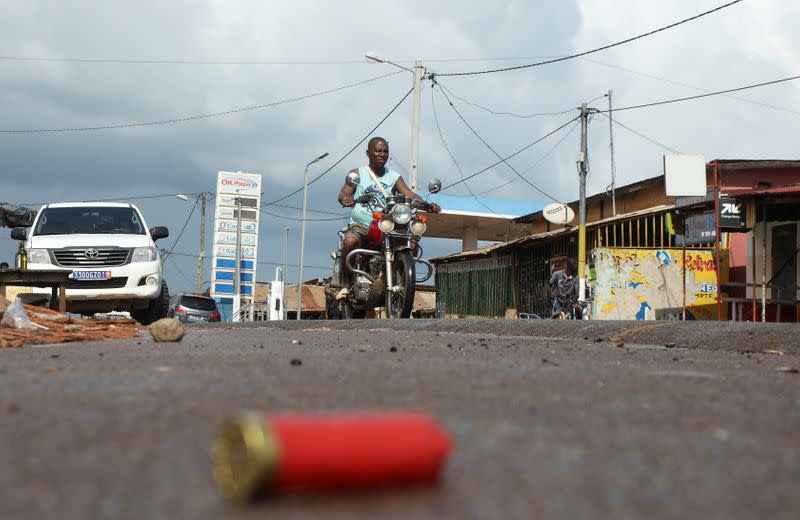 A man rides his motorcycle as a shotgun shell is seen on a street after post electoral inter-community clashes on Monday and Tuesday, in M'Batto